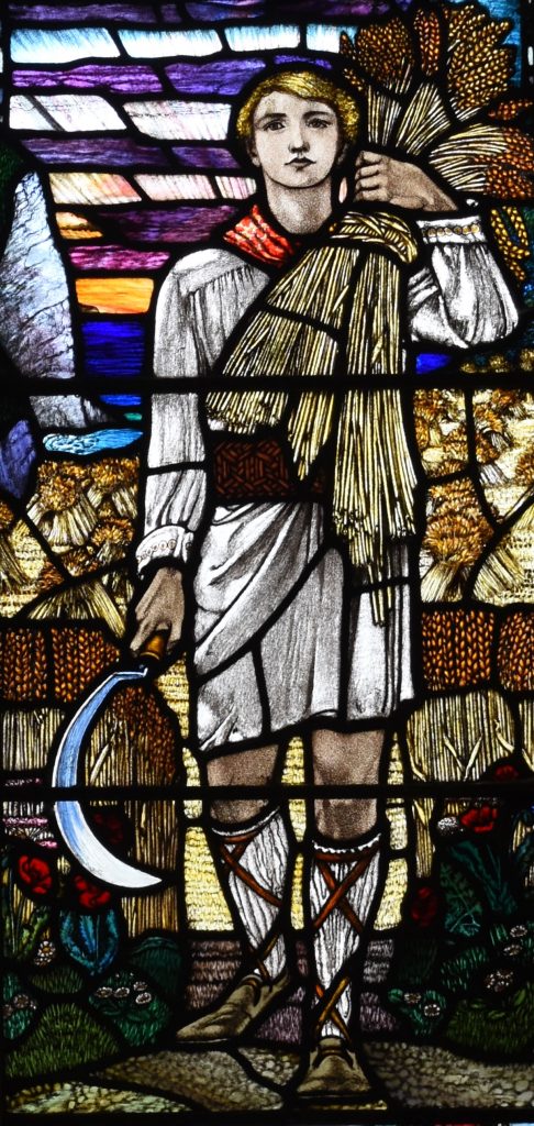 an Arts & Crafts stained glass window with the image of a young man carrying a sheaf of corn over his shoulder